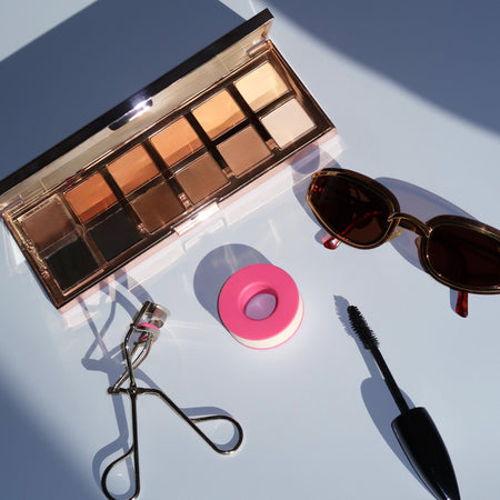 flat lay image showing eyeshadow palette, snatched tape, eyelash curlers and mascara